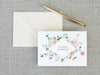 a card with a floral wreath on it next to a pen and envelope